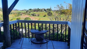 Um deck de madeira com mesa e cadeiras, com vista para uma paisagem verde com árvores e uma colina.