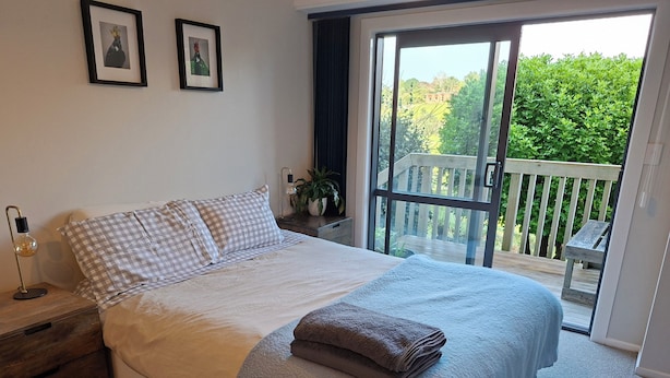 Quarto com cama, mesa de cabeceira, luminária, janela e varanda.