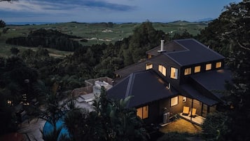 Une maison moderne dotée d’une grande terrasse et d’une piscine, entourée d’une végétation luxuriante et de collines.