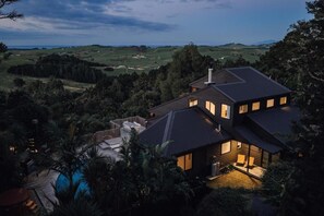 Ein modernes Haus mit einer großen Terrasse und einem Schwimmbad, umgeben von üppiger Vegetation und Hügeln.