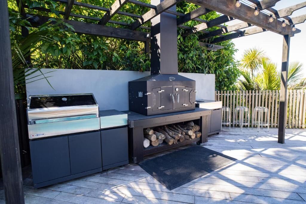 Cocina exterior con parrilla integrada, armarios de almacenamiento y una pérgola.