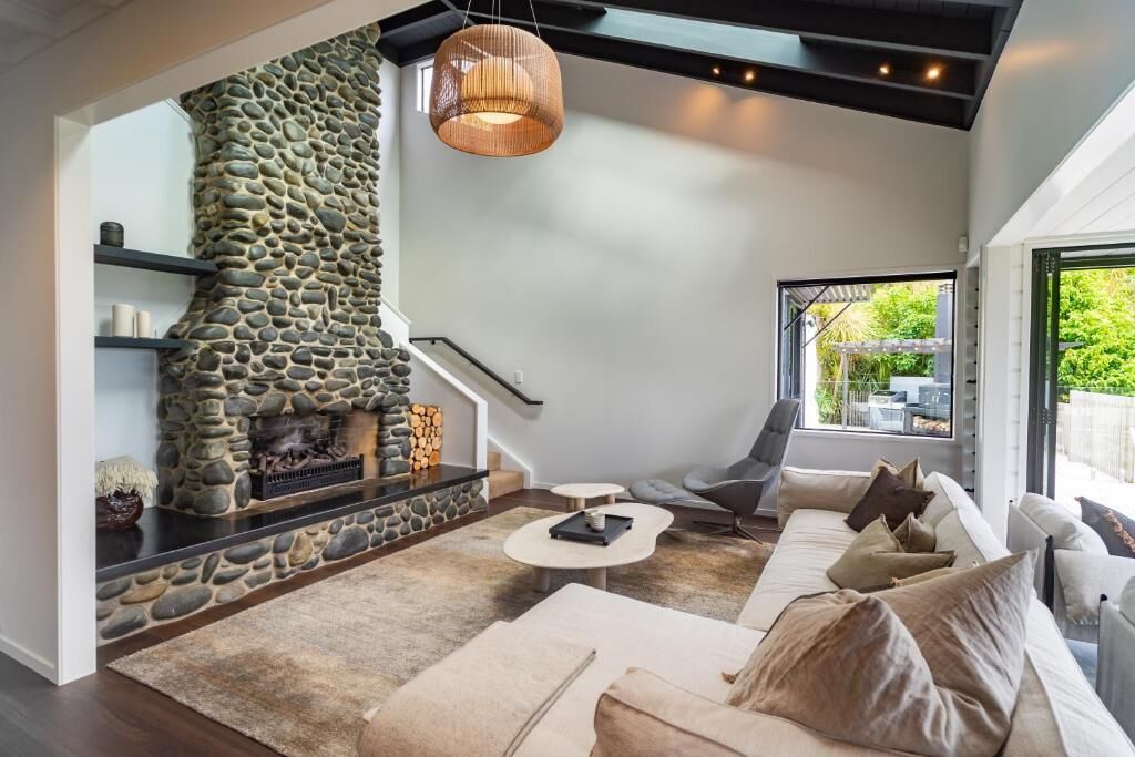 A modern living room with a stone fireplace, a sofa, a coffee table, and a hanging light fixture.