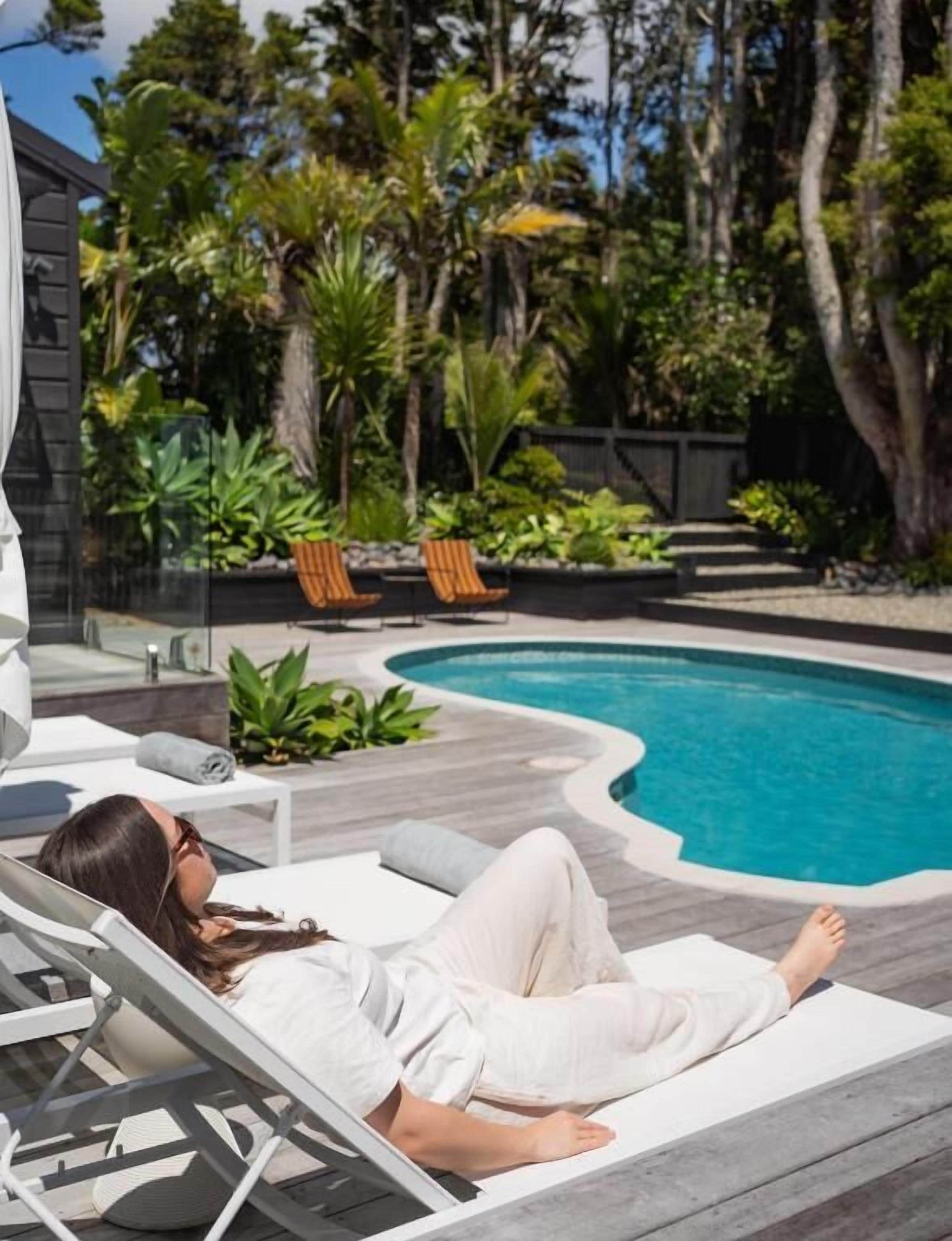 A poolside area with a lounge chair, a pool, and surrounding greenery.