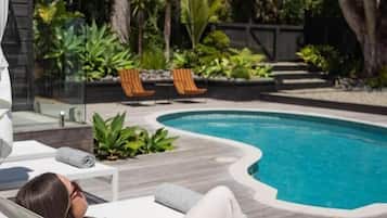 A poolside area with a lounge chair, a pool, and surrounding greenery.