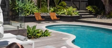 A poolside area with a lounge chair, a pool, and surrounding greenery.