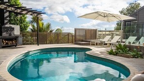 Una piscina con muelle de madera, sillas de descanso y una pérgola.