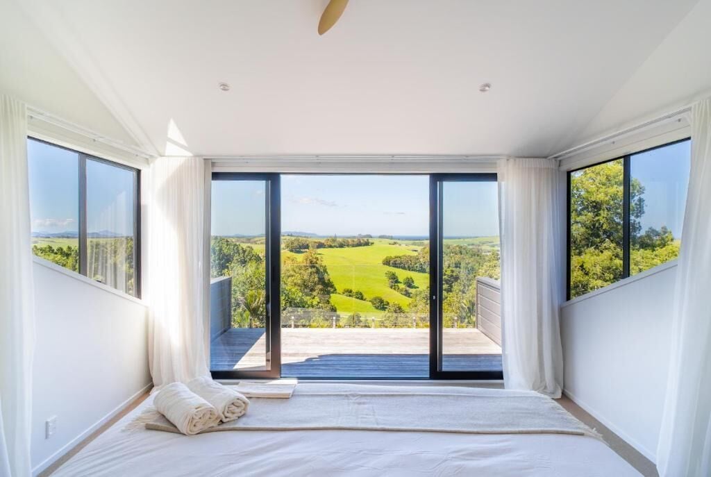 Quarto com cama grande, vista para paisagem verde através de porta deslizante e varanda.