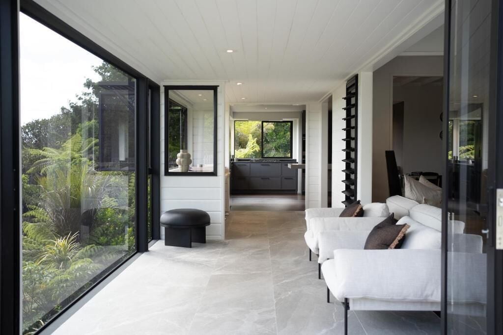 A modern interior with a sofa set, a glass partition, and a view of the outdoors.