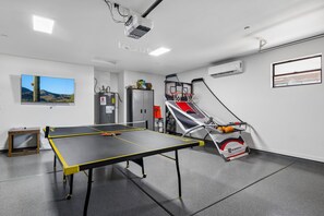 A room with a ping pong table, a basketball hoop, and a projector mounted on the ceiling. - The ONE | Pool, Game Room, & Putting Green | Old Town Scottsdale | Sleeps 10 (Scottsdale)