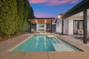 A swimming pool with a pergola and seating area, surrounded by a hedge and a modern building. - The ONE | Pool, Game Room, & Putting Green | Old Town Scottsdale | Sleeps 10 (Scottsdale)