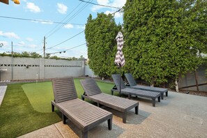 An outdoor seating area with lounge chairs and a striped umbrella. - The ONE | Pool, Game Room, & Putting Green | Old Town Scottsdale | Sleeps 10 (Scottsdale)
