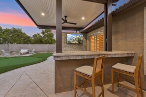 A covered outdoor area with a bar, two chairs, and a television screen.