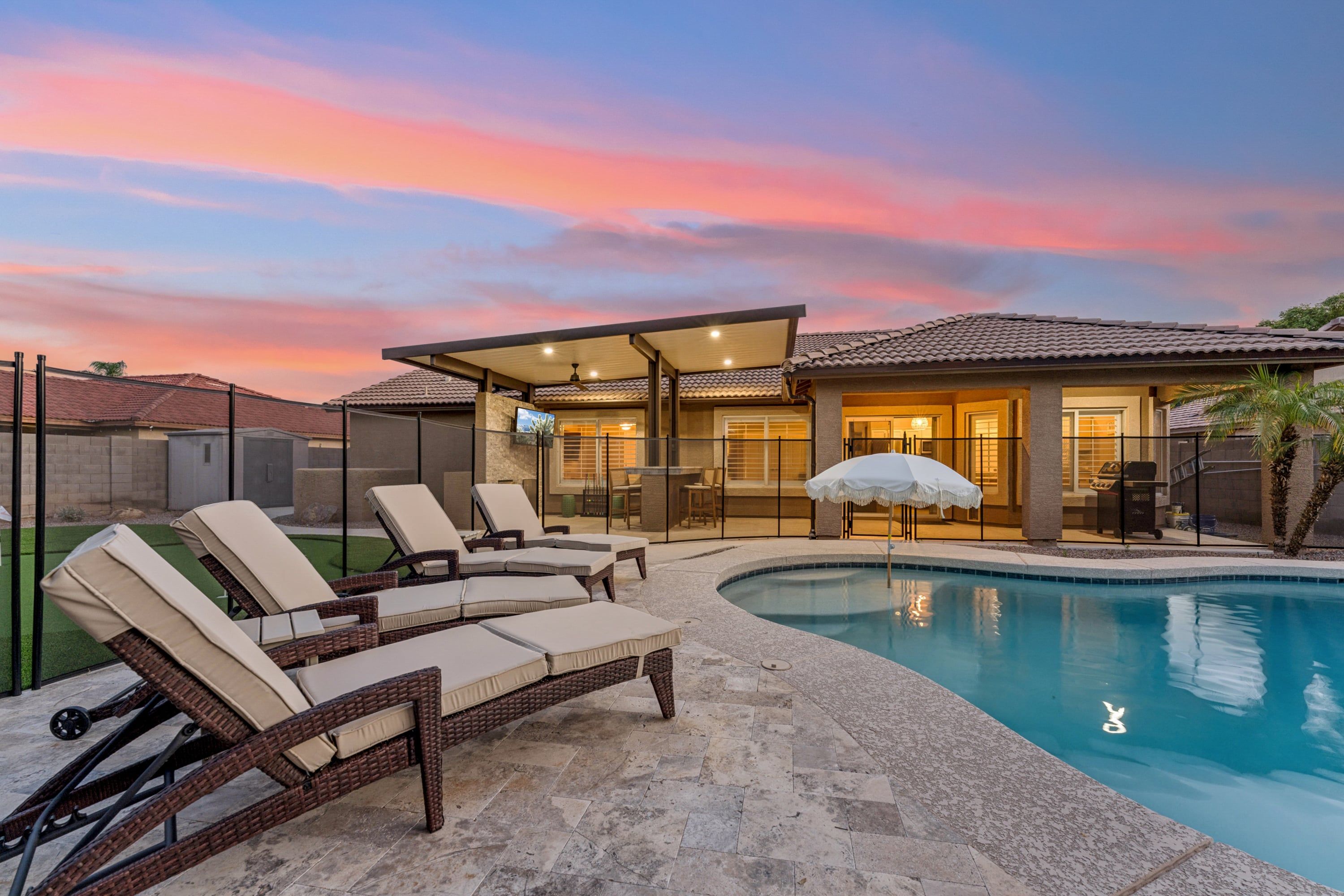 A residential property with a swimming pool, outdoor seating, and a covered patio area.