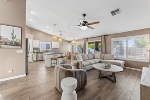 A spacious living area with a large sectional sofa, a round coffee table, and a dining area with a kitchen in the background.