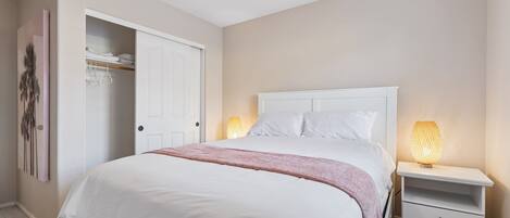 Un dormitorio con una cama, lámparas de noche, un armario y una puerta.