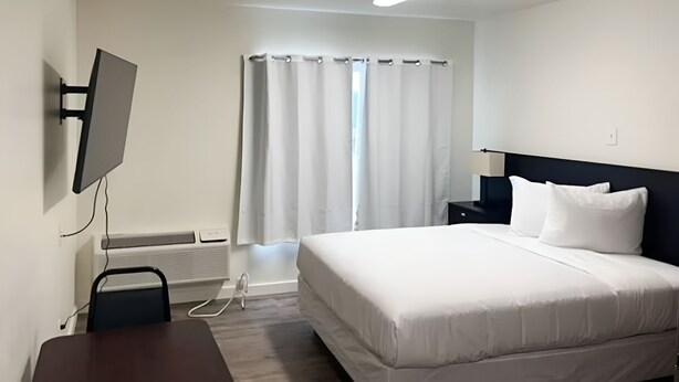 Habitación de hotel con cama, escritorio, silla, televisor montado en la pared y ventana con cortinas.