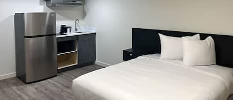 A hotel room with a bed, a kitchenette, and a refrigerator.