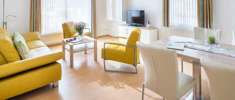 Una sala moderna con un sofá amarillo, una mesa de comedor y un televisor.