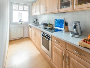 A modern kitchen with wooden cabinets, a built-in oven, a coffee maker, and a window with a view. - Marienstrasse 4a Apartment 4 (Norderney)