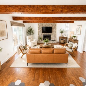 A modern living room with a stone fireplace, wooden beams, a large sofa, and a flat-screen TV.