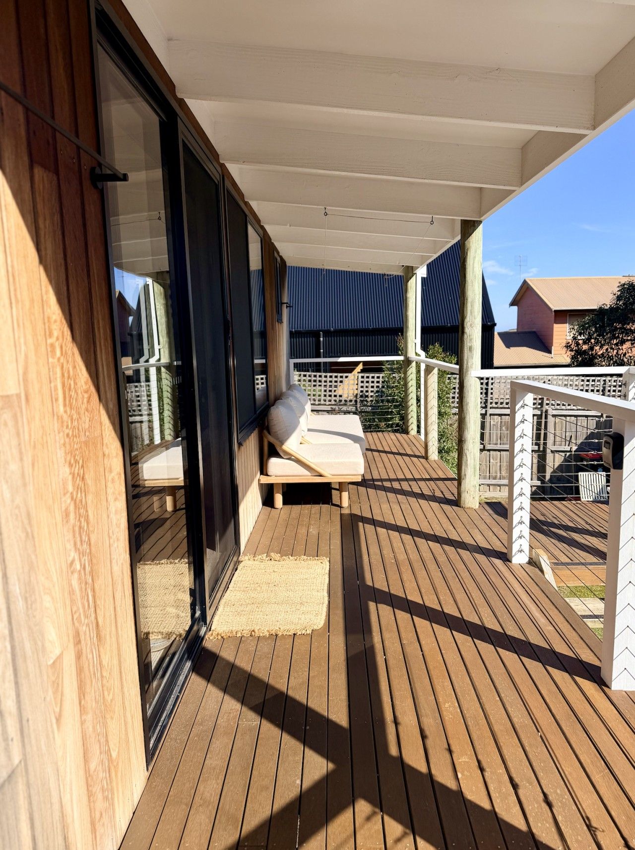 A wooden deck with a sliding glass door leading to a balcony, a cushioned lounge chair, and a small rug.