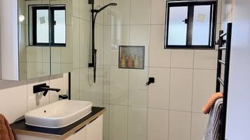 A modern bathroom with a white sink, a glass shower enclosure, and a large mirror.