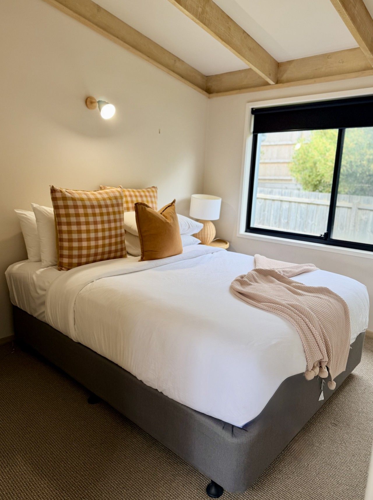 Un dormitorio con cama, almohadas, lámpara y ventana.