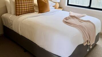 Un dormitorio con cama, almohadas, lámpara y ventana.