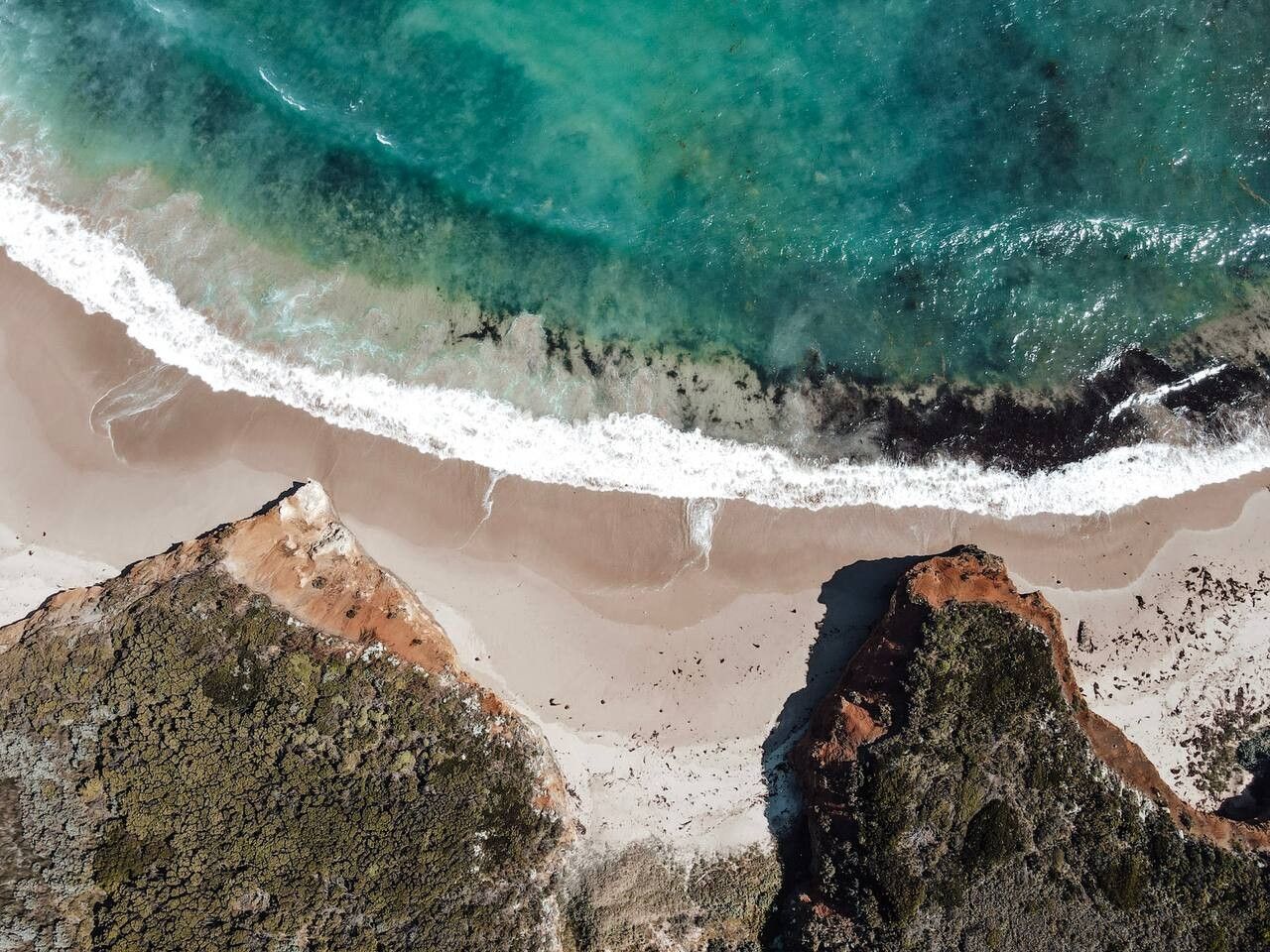 An aerial view of a beach with clear turquoise waters, sandy shore, and rocky outcrops.