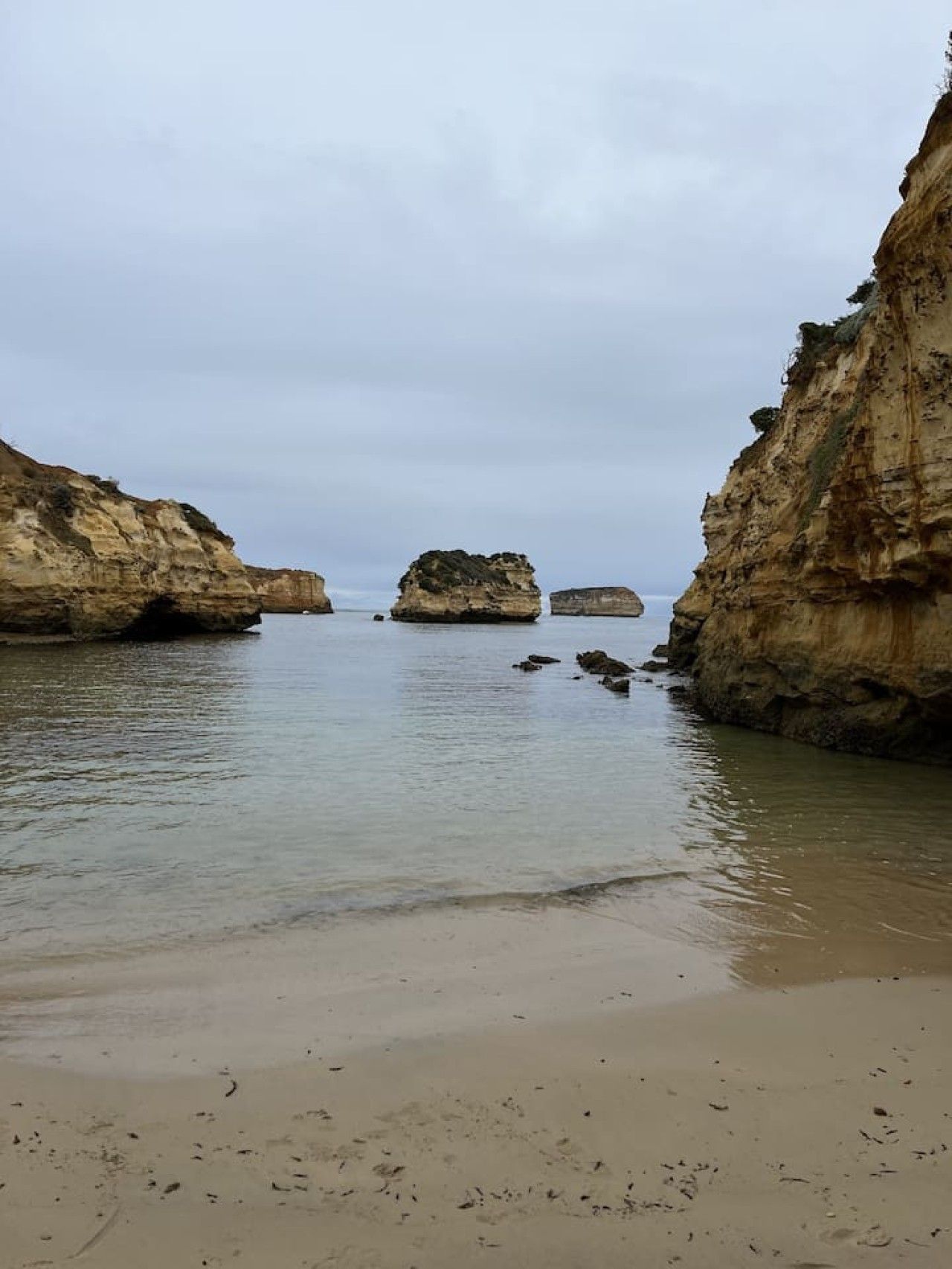 Un paisaje costero con mar tranquilo, playa de arena y acantilados rocosos.