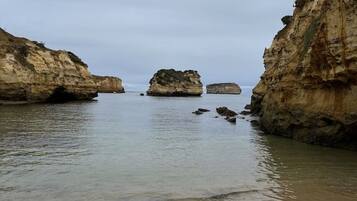 Un paisaje costero con mar tranquilo, playa de arena y acantilados rocosos.