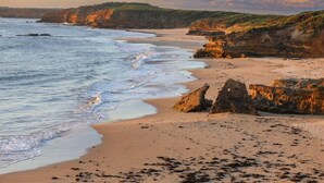 Ein Strand mit Wellen, felsigen Klippen und blauem Himmel.
