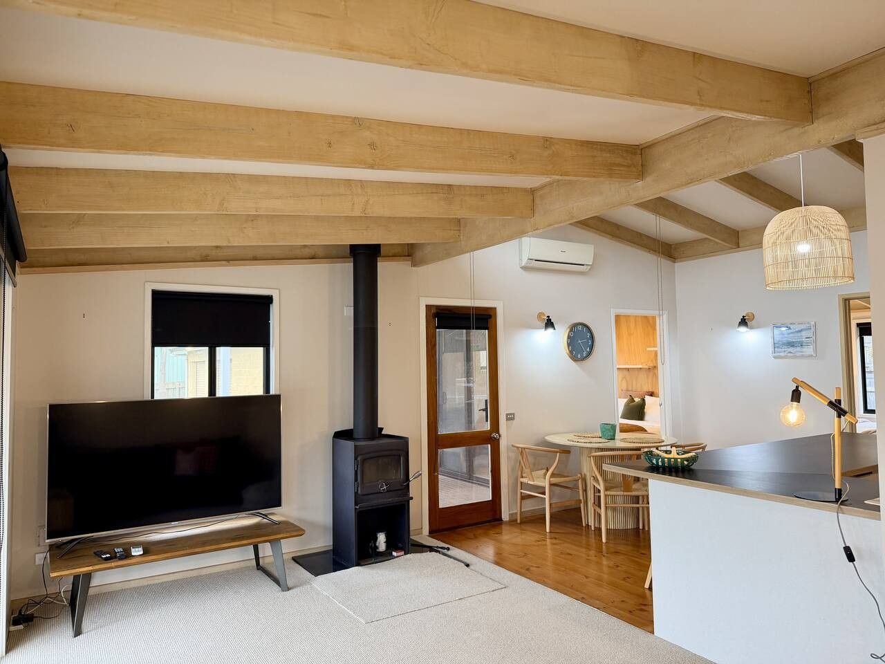 A living room with a television, a fireplace, a dining area with a table and chairs, and a kitchen area with a counter and pendant lighting.