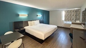 Habitación de hotel con cama, escritorio, silla, mesita de noche y ventana con cortinas estampadas.