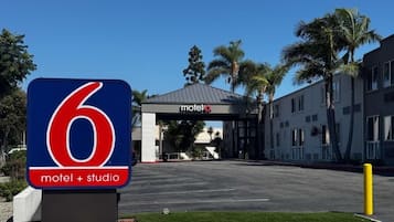 L’entrée d’un motel, avec un grand panneau indiquant le numéro 6, un espace de stationnement couvert et un bâtiment doté d’un toit plat.