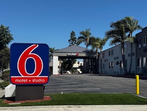 A motel entrance with a prominent number 6 sign, a covered parking area, and a building with a flat roof.