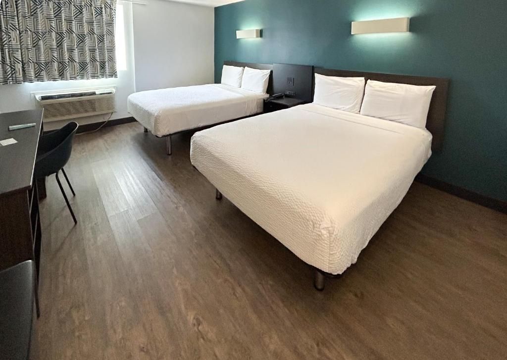 A hotel room with two beds, a desk, a chair, and a window with patterned curtains.