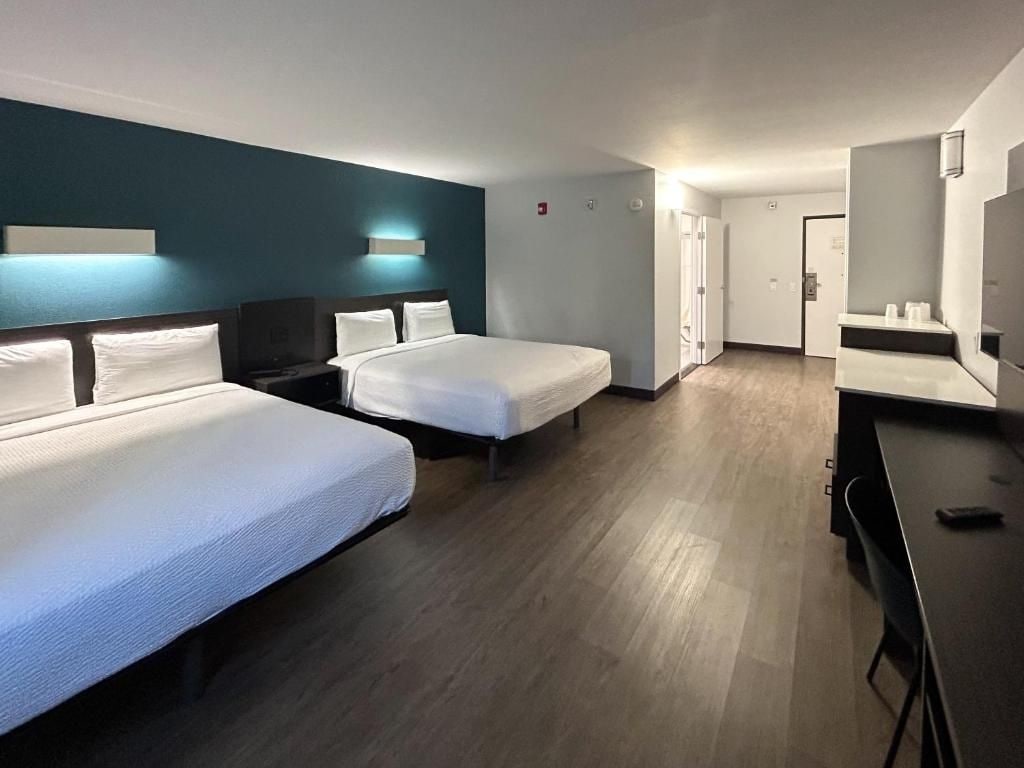 A hotel room with two beds, a desk, a chair, a TV, and a bathroom door.