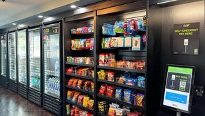 Un’area di self-checkout con un terminale di pagamento digitale e scaffali pieni di snack e bevande.