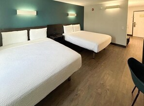 Habitación de hotel con dos camas, una mesita de noche y una silla.