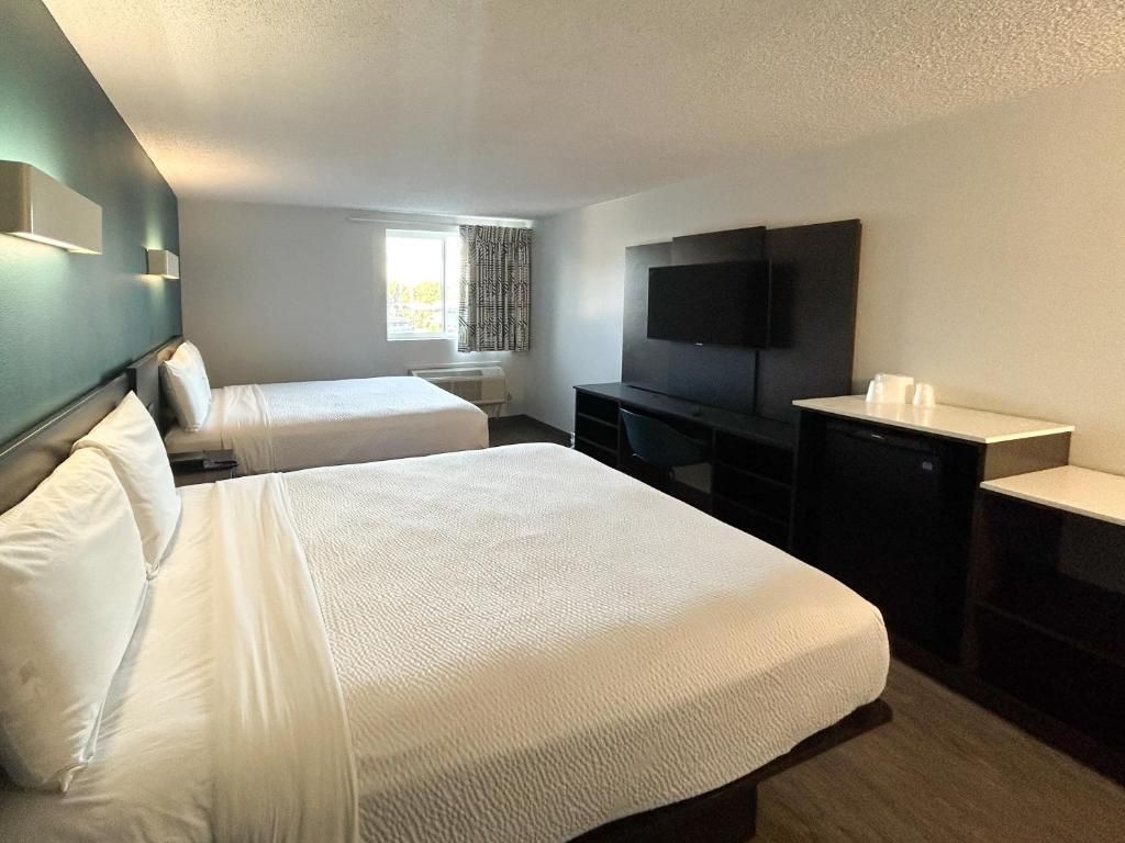 A hotel room with two beds, a flat-screen TV, a desk, and a window with curtains.