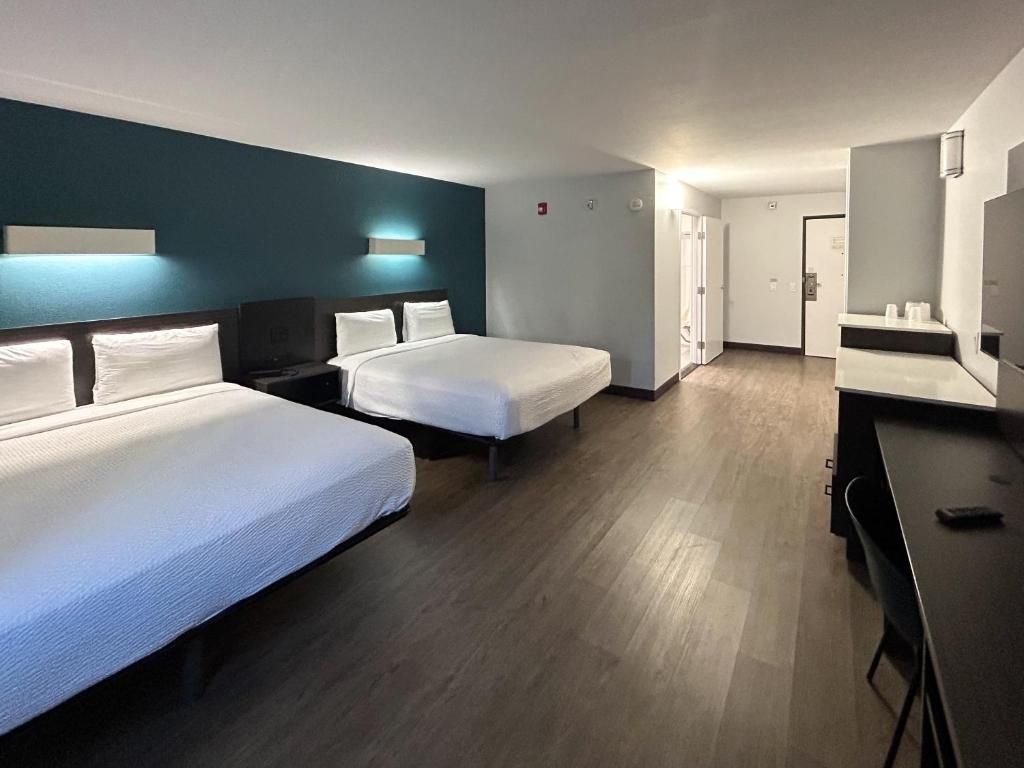 A hotel room with two beds, a desk, a chair, a TV, and a bathroom door.