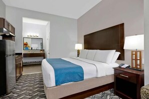 Una habitación de hotel con una cama, mesita de noche, lámpara y vistas al baño.