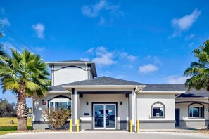 Un edificio de dos plantas con un porche, garaje y una pequeña construcción adosada con ventana.