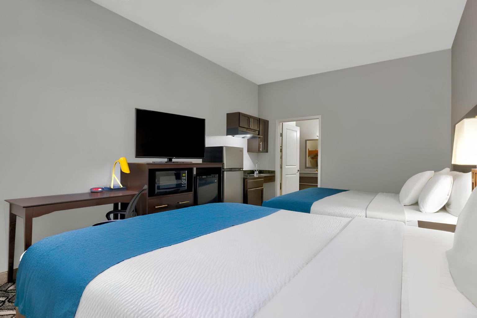 A hotel room with two beds, a desk with a computer, a television, and a kitchenette.