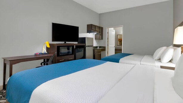 Ein Hotelzimmer mit zwei Betten, einem Schreibtisch mit Computer, einem Fernseher und einer Küchenzeile.