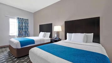 A hotel room with two beds, a window with patterned curtains, a nightstand with a lamp, and a patterned carpet.