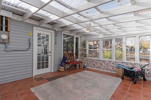 A sunroom with a large window, a door, a chair, a rug, and a small table with items on it. - Peaceful 3-bedroom lake house with hot tub, and sauna.Birders paradise. (Amherstburg)