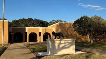 Un edificio con fachada de ladrillo, un camino que lleva a una entrada y una estatua de un gato sobre un pedestal.