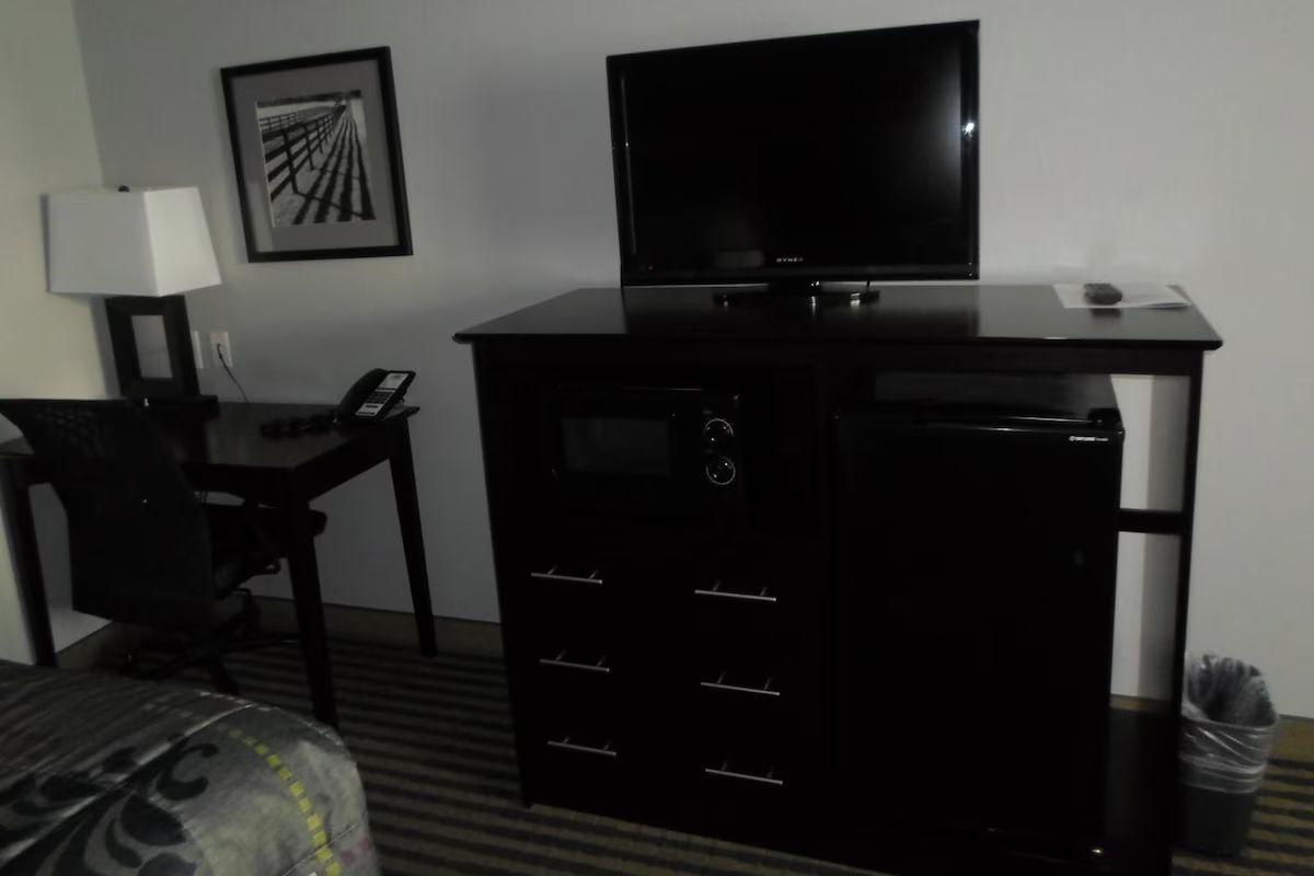 Habitación de hotel con televisión de pantalla plana, escritorio con lámpara, una silla y cama con cubrecama estampado.
